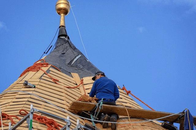 Worker sitting on scaffolding on a roof. 