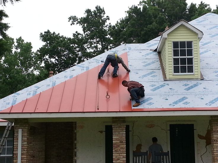 Workers installing a standing seam roof system on a house.