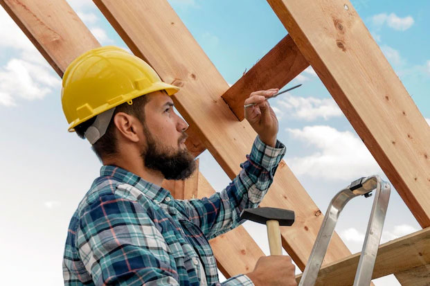 Construction working driving nails into a rafter.