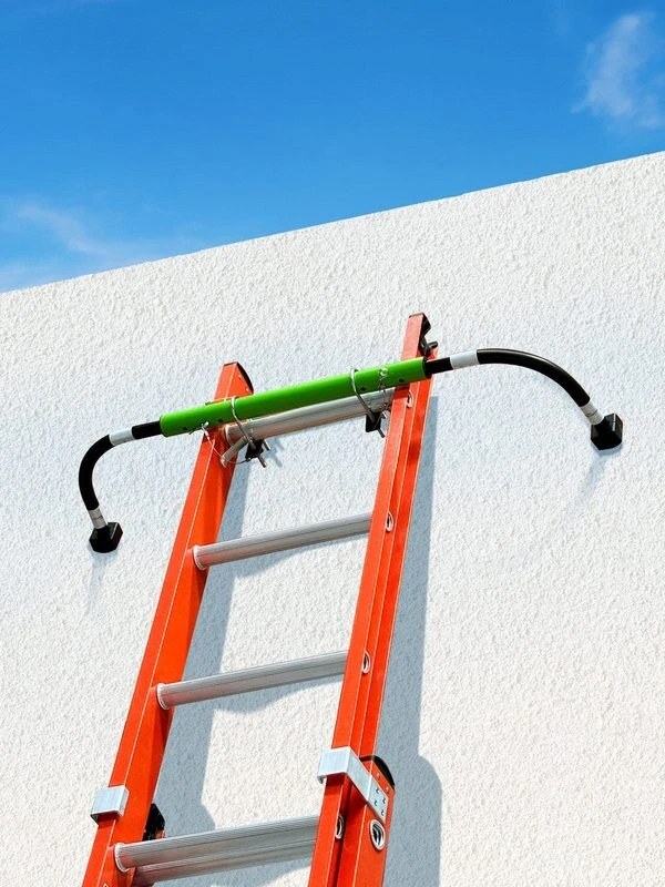 Frontline LAS48 universal ladder stabilizer clamped near the top of an extension ladder against a wall, its curved arms holding the rails off the wall and widening the contact for a stable setup. Frontline LAS48 universal ladder stabilizer clamped near the top of an extension ladder against a wall, its curved arms holding the rails off the wall and widening the contact for a stable setup.